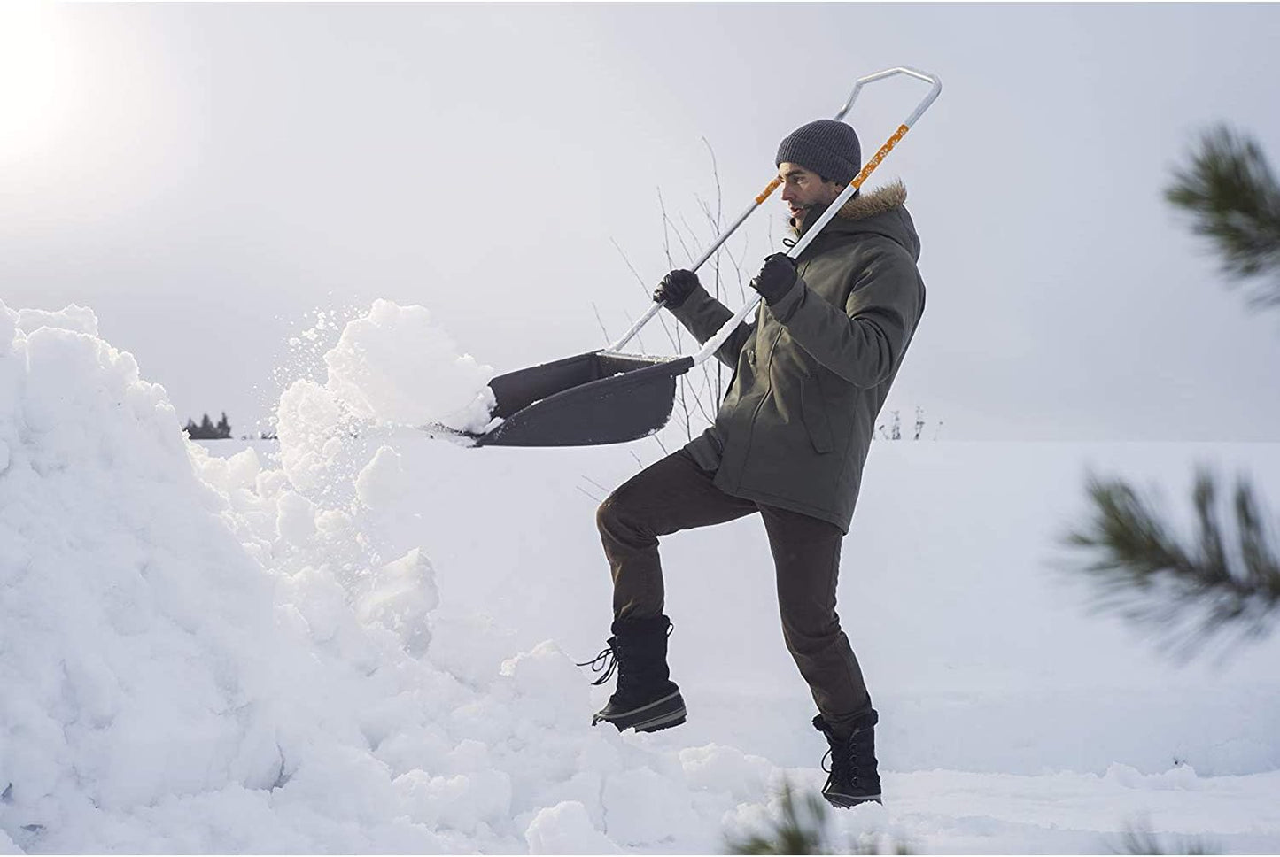 Uomo che spalare la neve con una pala ergonomica in una giornata invernale, indossando giacca invernale, berretto e guanti. Attrezzo da neve resistente per rimuovere facilmente grandi quantità di neve. Ideale per condizioni climatiche fredde.