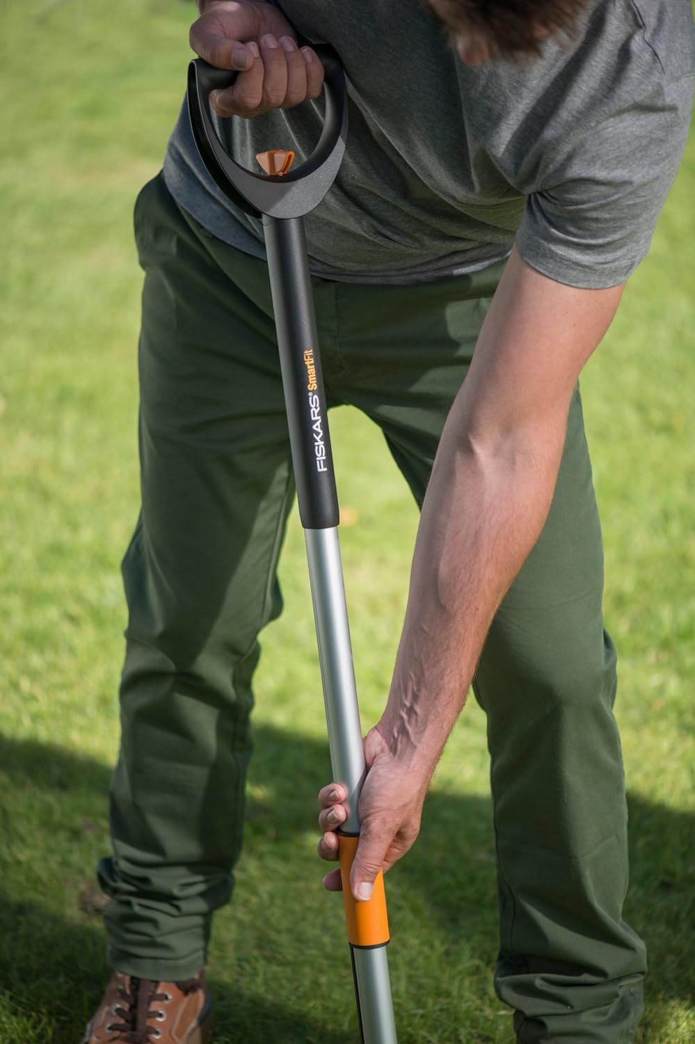 Uomo usa attrezzo da giardinaggio Fiskars SmartFit per lavori all'aperto. Pala ergonomica con impugnatura comoda e regolabile, ideale per giardinaggio e cura del prato. Attrezzo resistente e di qualità per giardinieri amatoriali e professionisti.