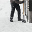 Persona che spalare neve con pala Fiskars, pantaloni neri e guanti invernali, davanti a una casa in legno. Strumento ideale per la rimozione della neve in inverno.