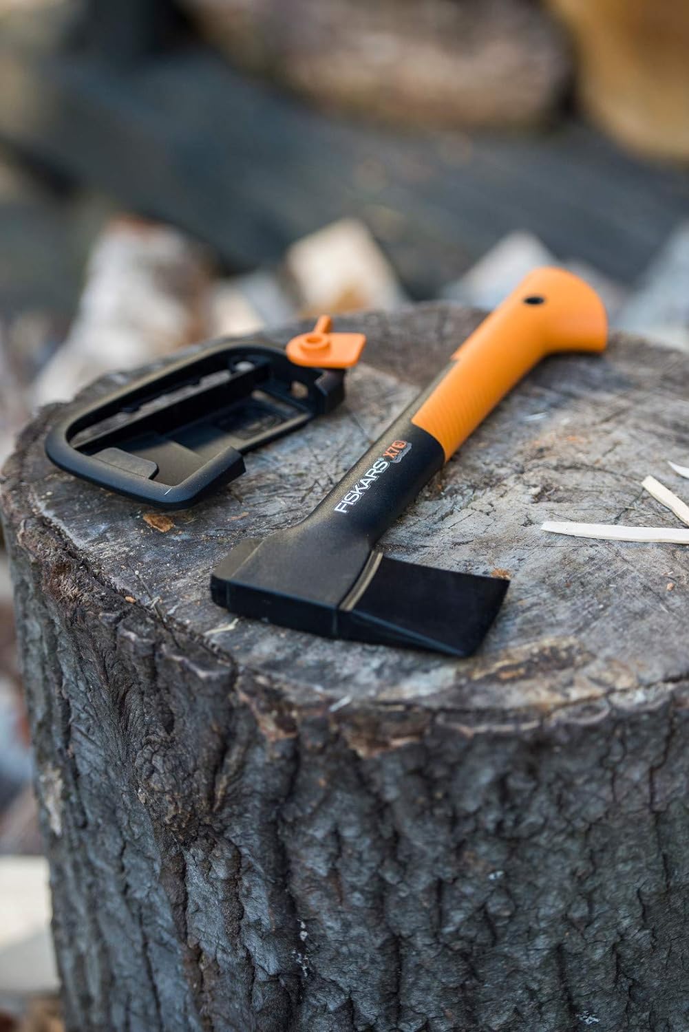 Ascia Fiskars X7 con manico arancione e nero, posata su un ceppo di legno, ideale per il campeggio e le attività all'aperto, con custodia protettiva. Strumento resistente e leggero per taglio e spacco di legna.