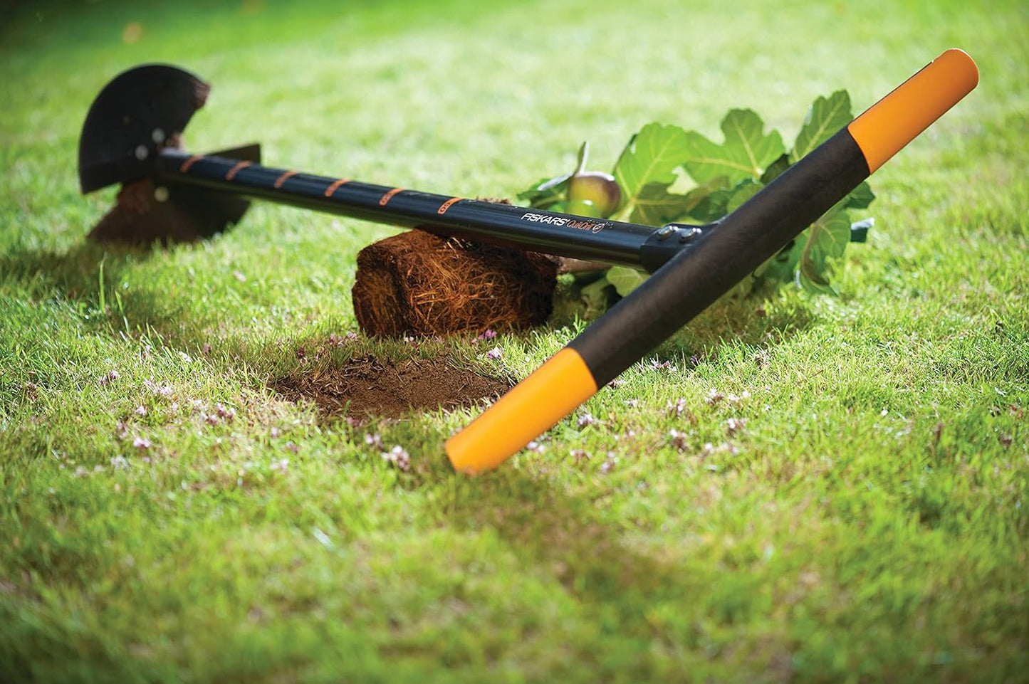 Attrezzo da giardinaggio Fiskars QuikDrill con manico ergonomico arancione e nero, ideale per piantare, aerare il terreno e rimuovere erbacce. Perfetto per lavori di giardinaggio su prato verde. Efficiente e facile da usare.