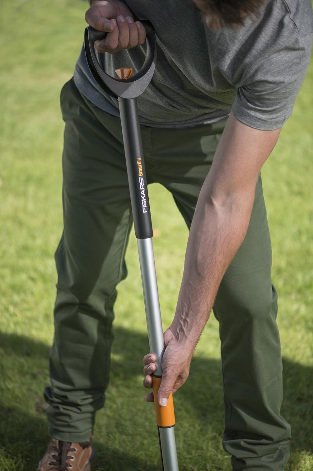 Uomo utilizza un estirpatore di erbacce Fiskars SmartFit in giardino. Attrezzo da giardinaggio ergonomico con impugnatura comoda e regolabile. Ideale per rimuovere facilmente le erbacce senza piegarsi. Strumento essenziale per la cura del prato.