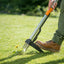 Uomo utilizza un estirpatore di erbacce con manico lungo su un prato verde. Strumento da giardinaggio ergonomico con impugnatura arancione e scarpe robuste. Ideale per rimuovere erbacce senza piegarsi, mantenendo il prato curato e sano.