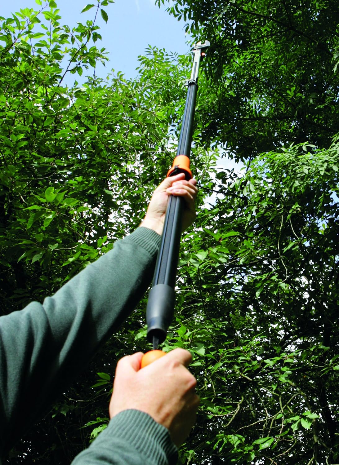 Persona che utilizza un potatore telescopico per tagliare rami alti in un giardino. Strumento per la potatura di alberi e arbusti, ideale per giardinaggio e manutenzione del verde. Manico ergonomico e lama affilata per tagli precisi e sicuri.