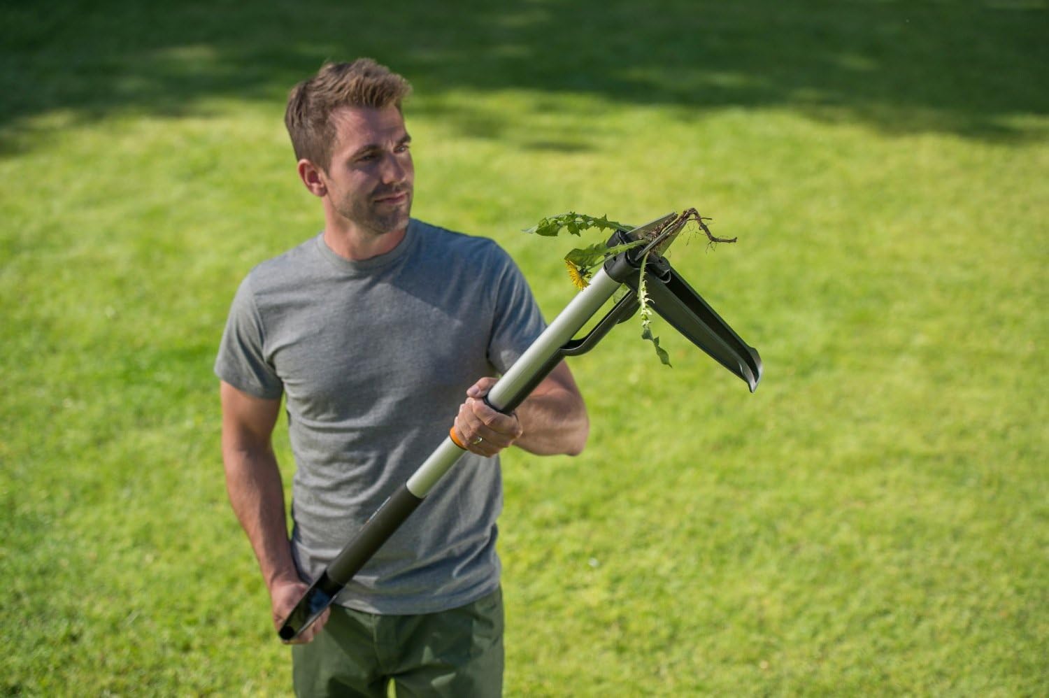 Uomo in giardino utilizza un estirpatore di erbacce ergonomico per rimuovere piante indesiderate. Strumento da giardinaggio con manico lungo e pinza per una facile e comoda rimozione delle erbacce. Ideale per mantenere il prato pulito e ordinato.