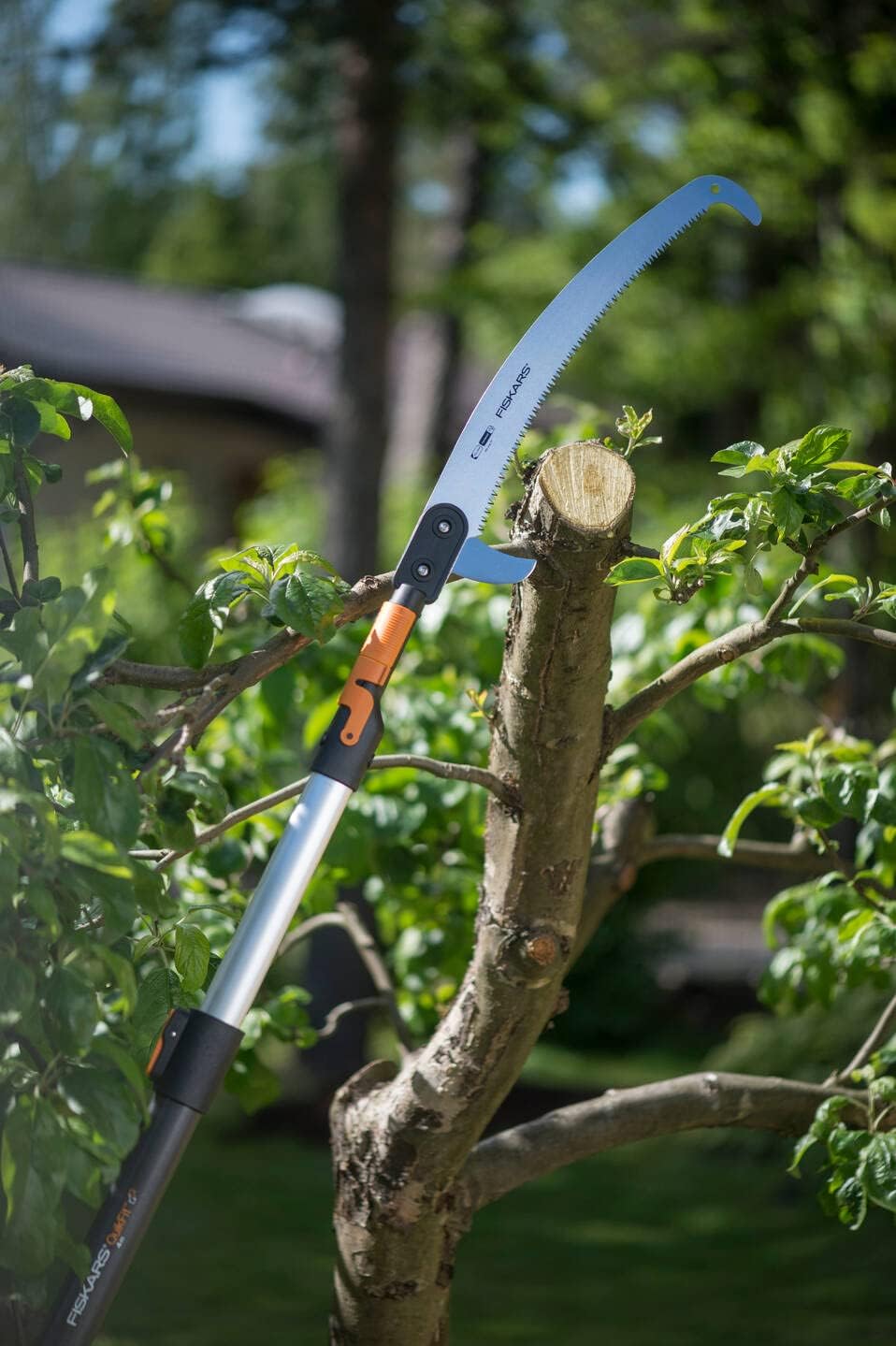 Sega da potatura telescopica Fiskars in azione su un ramo di albero. La lama curva e affilata taglia facilmente il legno, ideale per giardinaggio e manutenzione degli alberi. Strumento robusto e ergonomico per tagli precisi e sicuri.