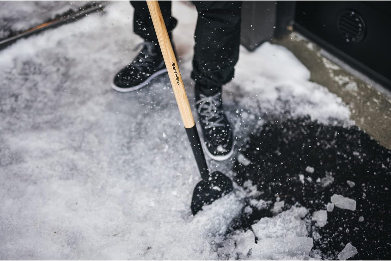 Rimozione della neve con pala Fiskars su vialetto ghiacciato, attrezzo da giardino con manico in legno e punta in metallo, scarpe invernali nere, attrezzatura per la pulizia della neve, strumenti per l'inverno, sicurezza invernale.