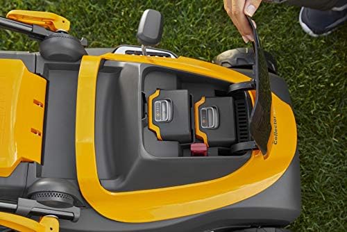 Tagliaerba elettrico giallo con vano batteria aperto, mostrando due batterie ricaricabili. Una mano sta sollevando il coperchio del vano. Il tagliaerba è posizionato su erba verde. Design ergonomico e compatto per una facile manutenzione del giardino.